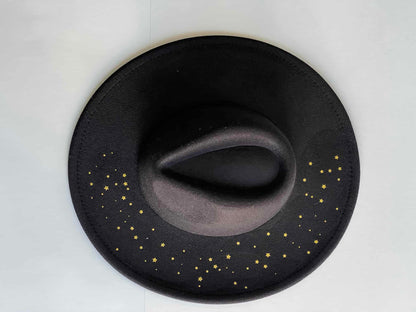 ¡Añade un toque de elegancia y originalidad a tu outfit con Noche Estrellada, el sombrero fedora en negro con detalles dorados! Este sombrero es imprescindible para aquellos que buscan un toque de sofisticación en su look.
